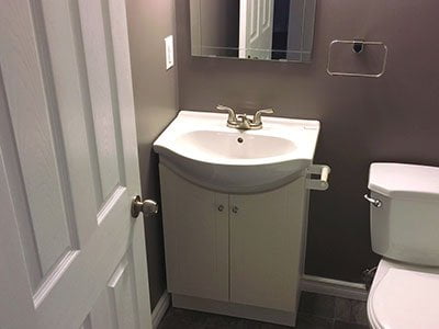 Guest bathroom with brown painted walls, small white cabinet with sink, small mirror, and white door.