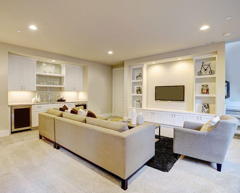 Basement entertainment room with beige couches, light beige carpet floor, white shelves, LED lighting, and flat screen TV.