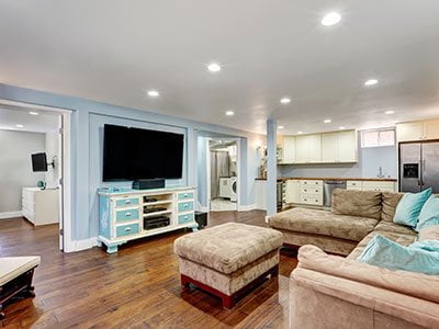 Large basement entertainment room with blue painted walls, wooden floor, beige couch, flat screen TV, and LED lighting.