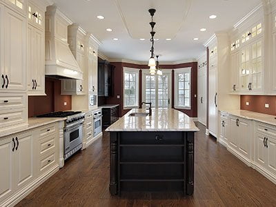 Modern kitchen with white cabinets, wooden island, white countertop, wooden floor, and warm lighting.