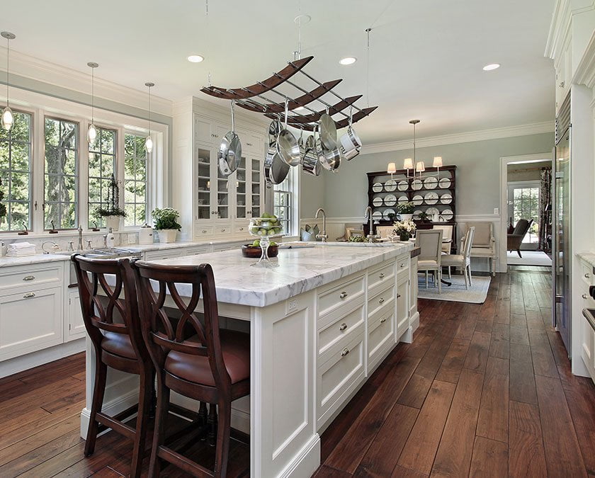 Modern kitchen with white cabinets, wooden floor, large white island with wooden chairs, modern lighting, and wide windows.