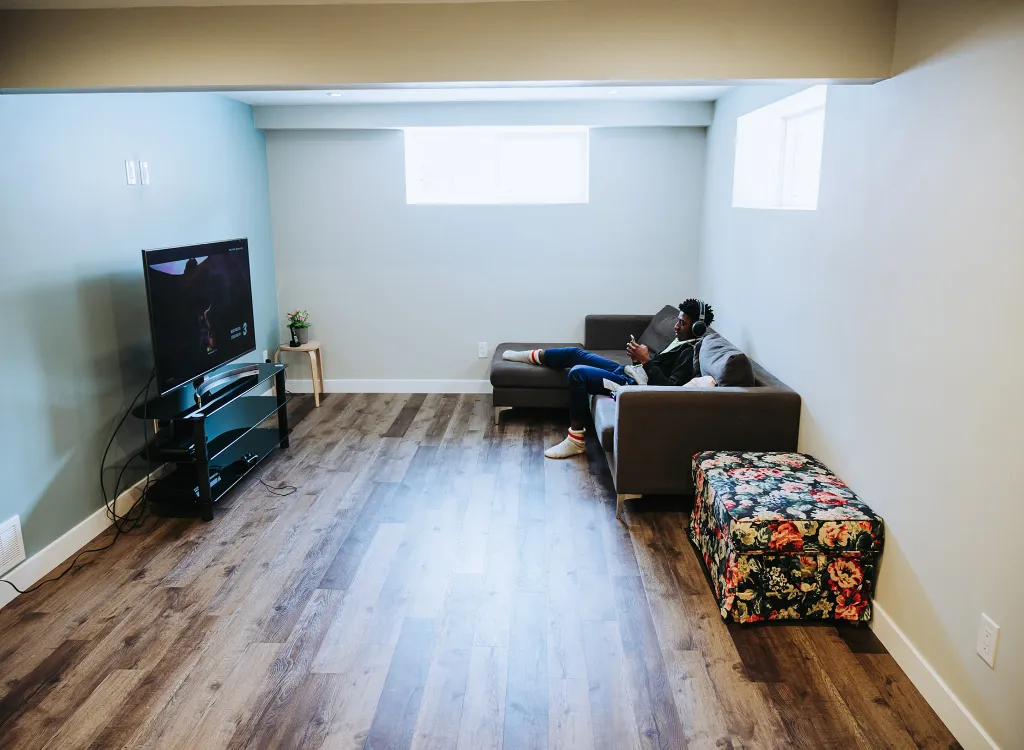 A young man watches television from a couch in a sports lounge basement design remodel.